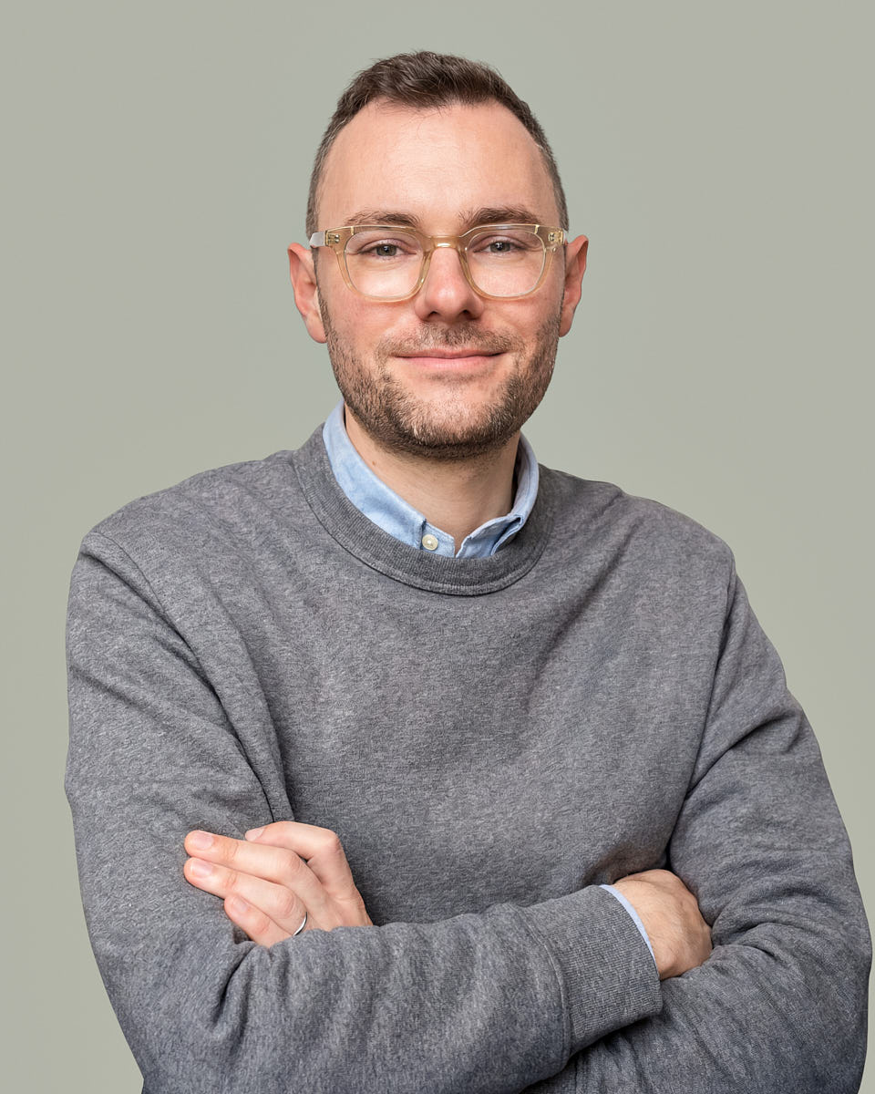 Enterprise headshot of a man in a gray sweater with a relaxed professional stance.