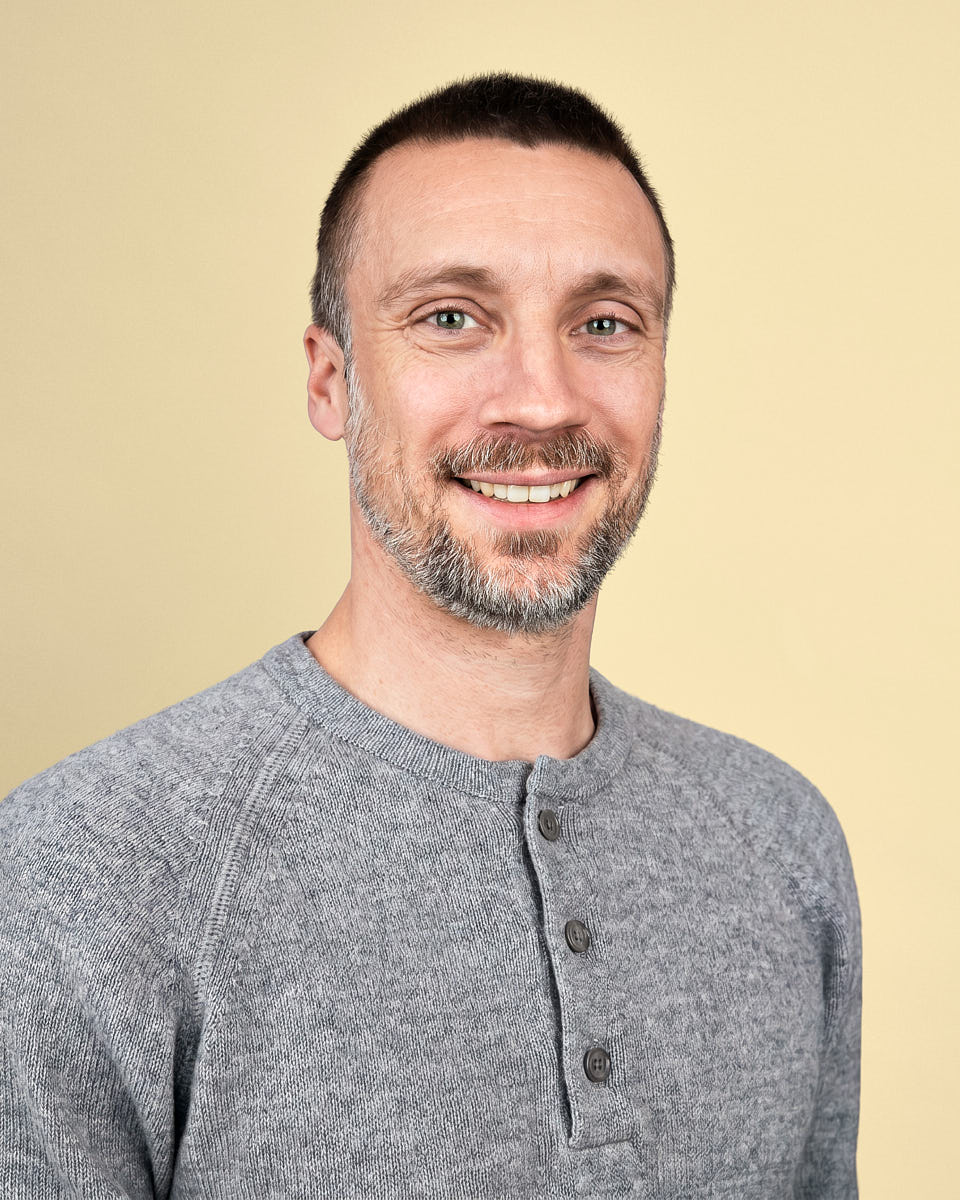 Modern executive headshot of a man in a gray henley with a warm professional background.