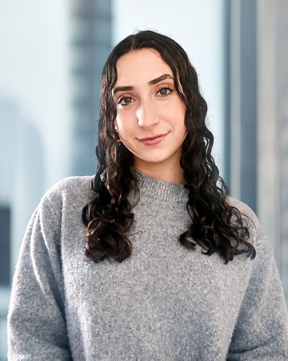 Softly lit executive headshot of a woman in a gray sweater with a clean professional background.