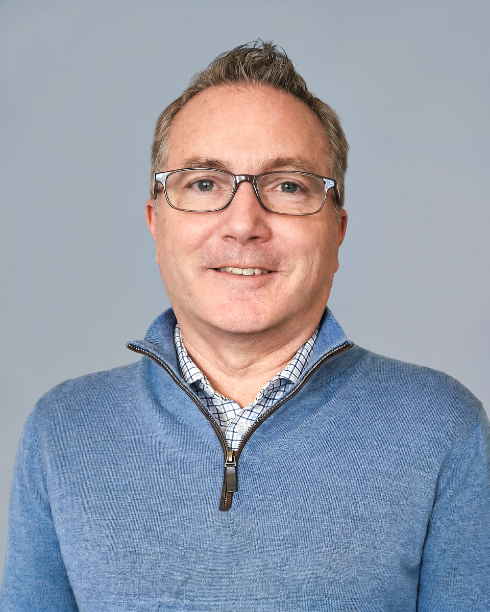 Consistent onboarding headshot of a man in a blue sweater against a clean gray background.