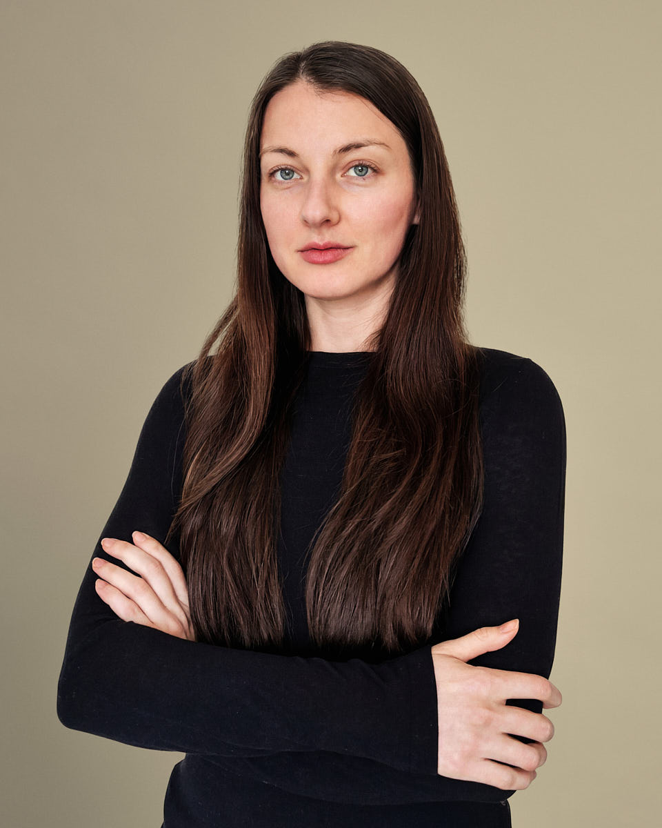 Clean new employee portrait of a woman in a black top with a simple neutral backdrop.
