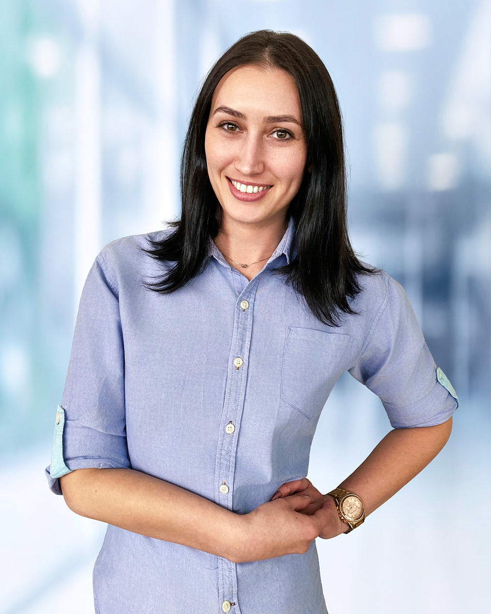 Virtual headshot example of a woman in a light blue shirt with a bright office-style background.